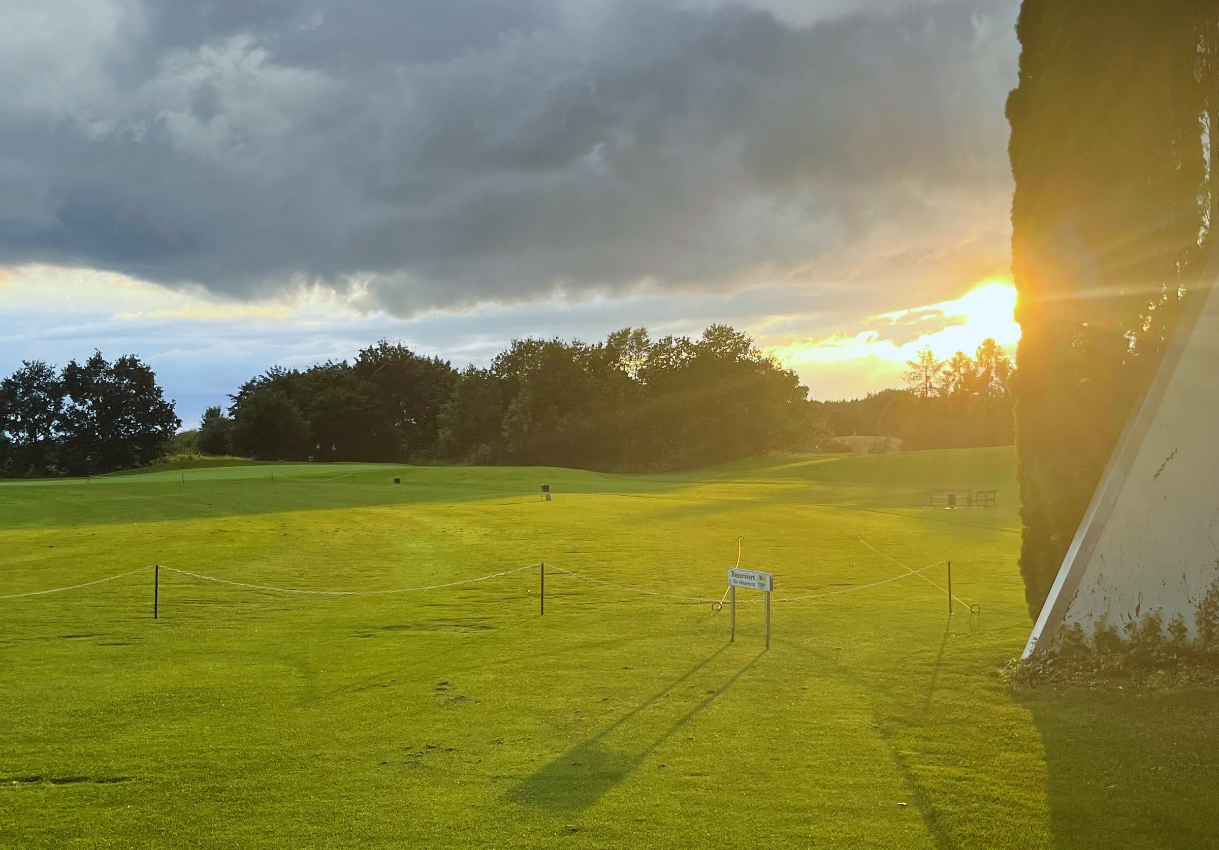 Fairway im Abendlicht, die Sonne steht tief hinter der Baumreihe