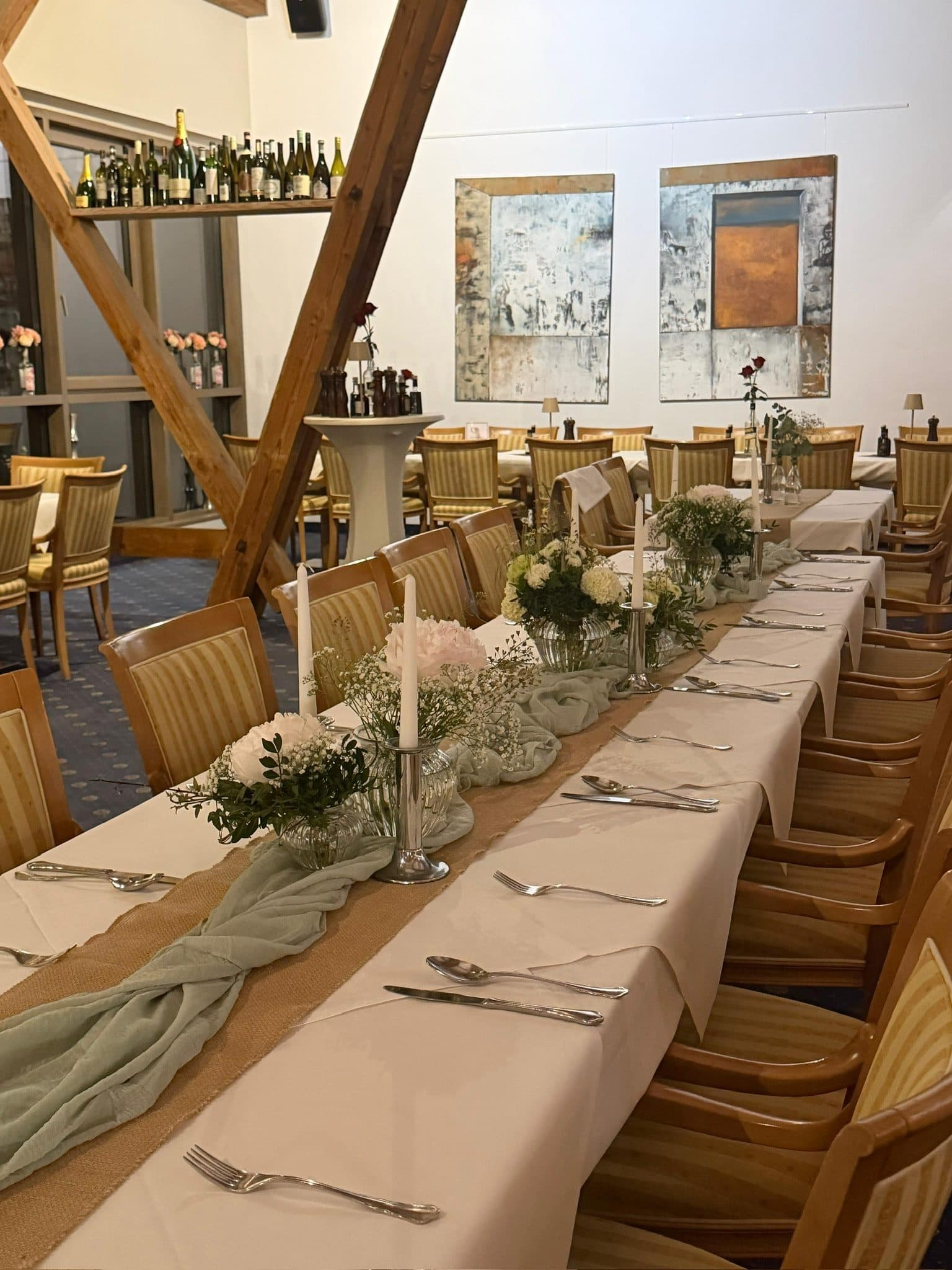 Lange Festtafel mit weißen Blumen, Kerzen und Tischläufer unter dem Dachstuhl