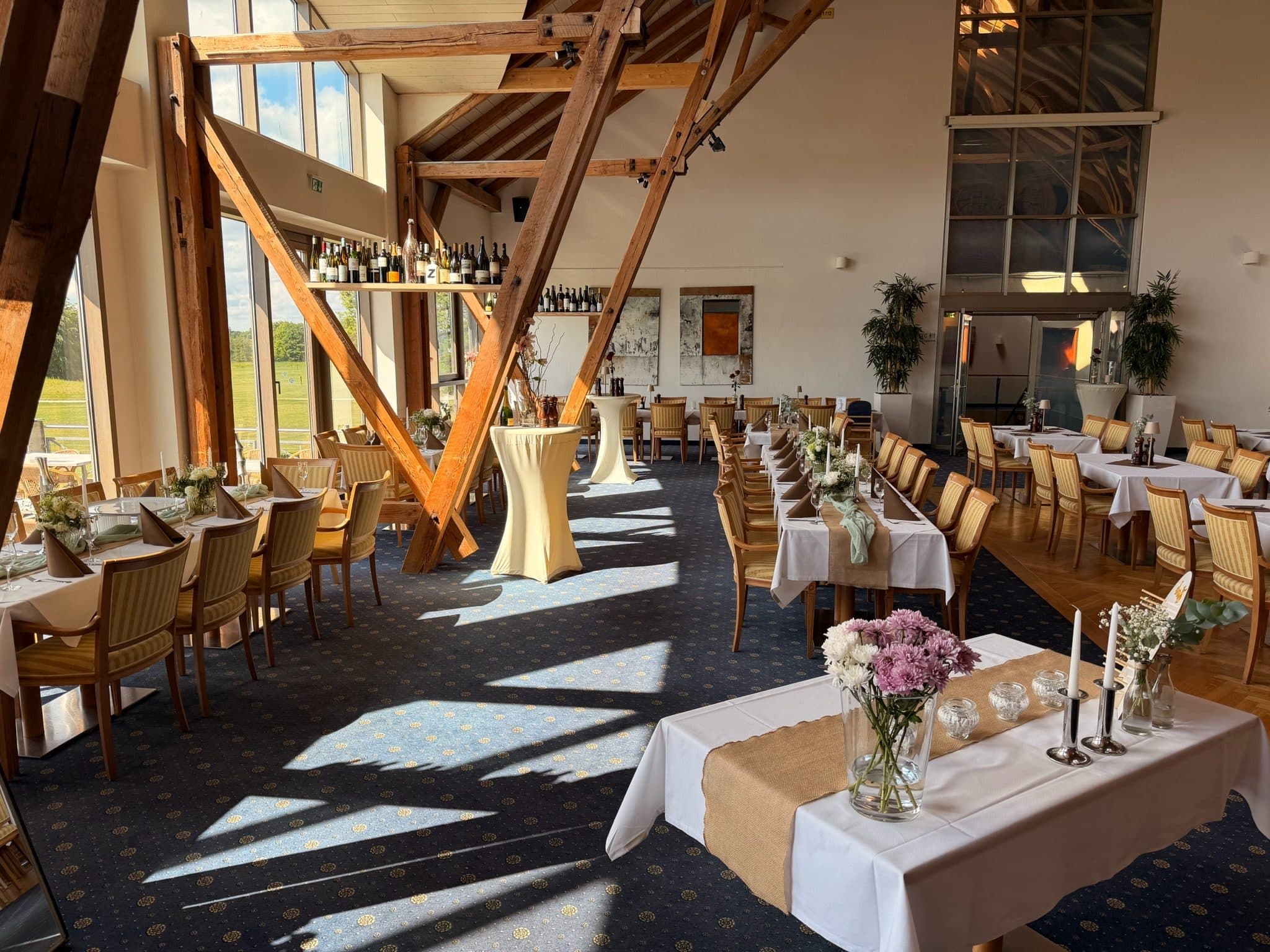 The dining room beneath the open timber roof, sunlight falling through the tall windows onto the laid tables