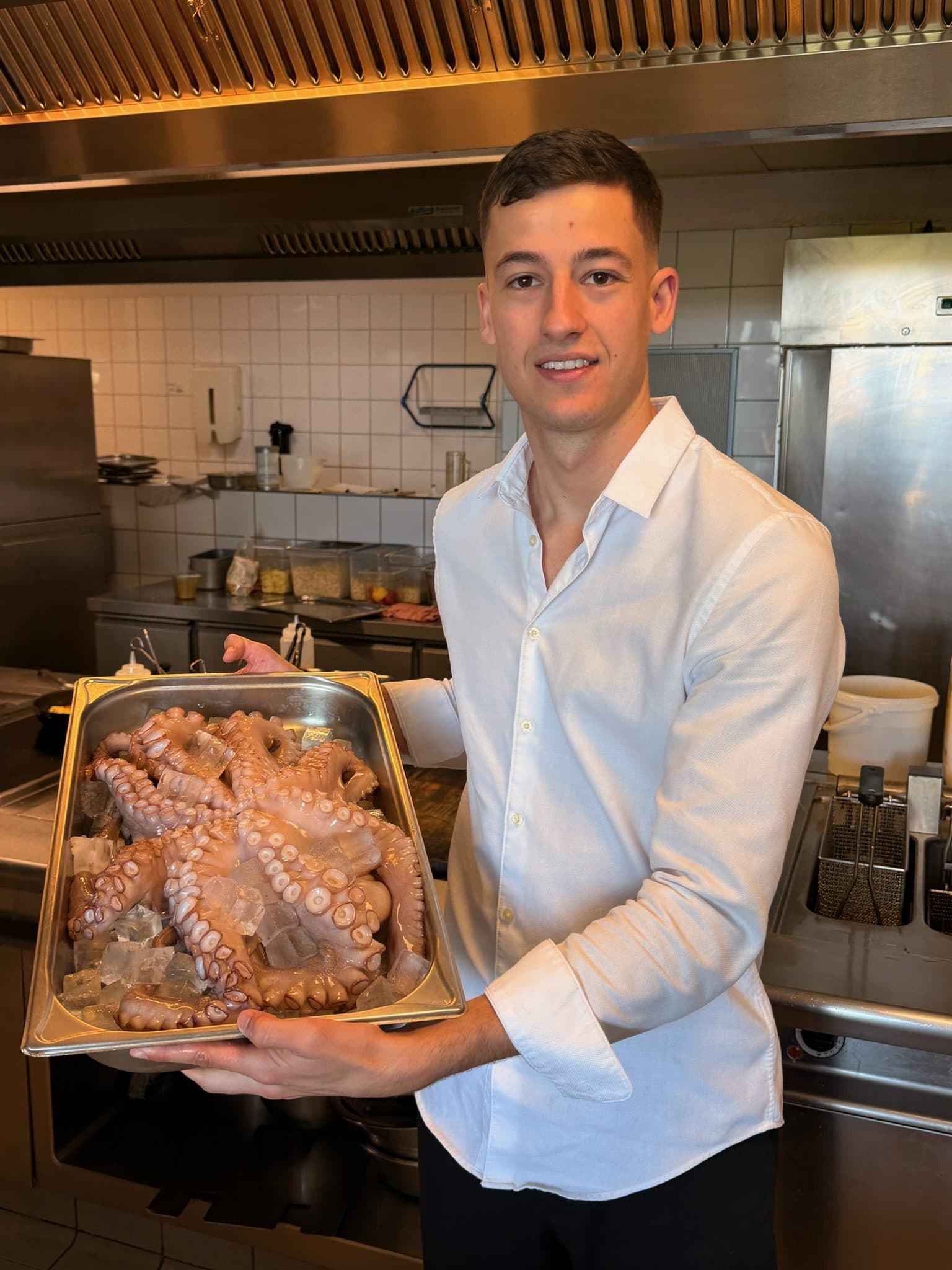 Ein Koch hält in der Küche eine Schale mit frischem Oktopus