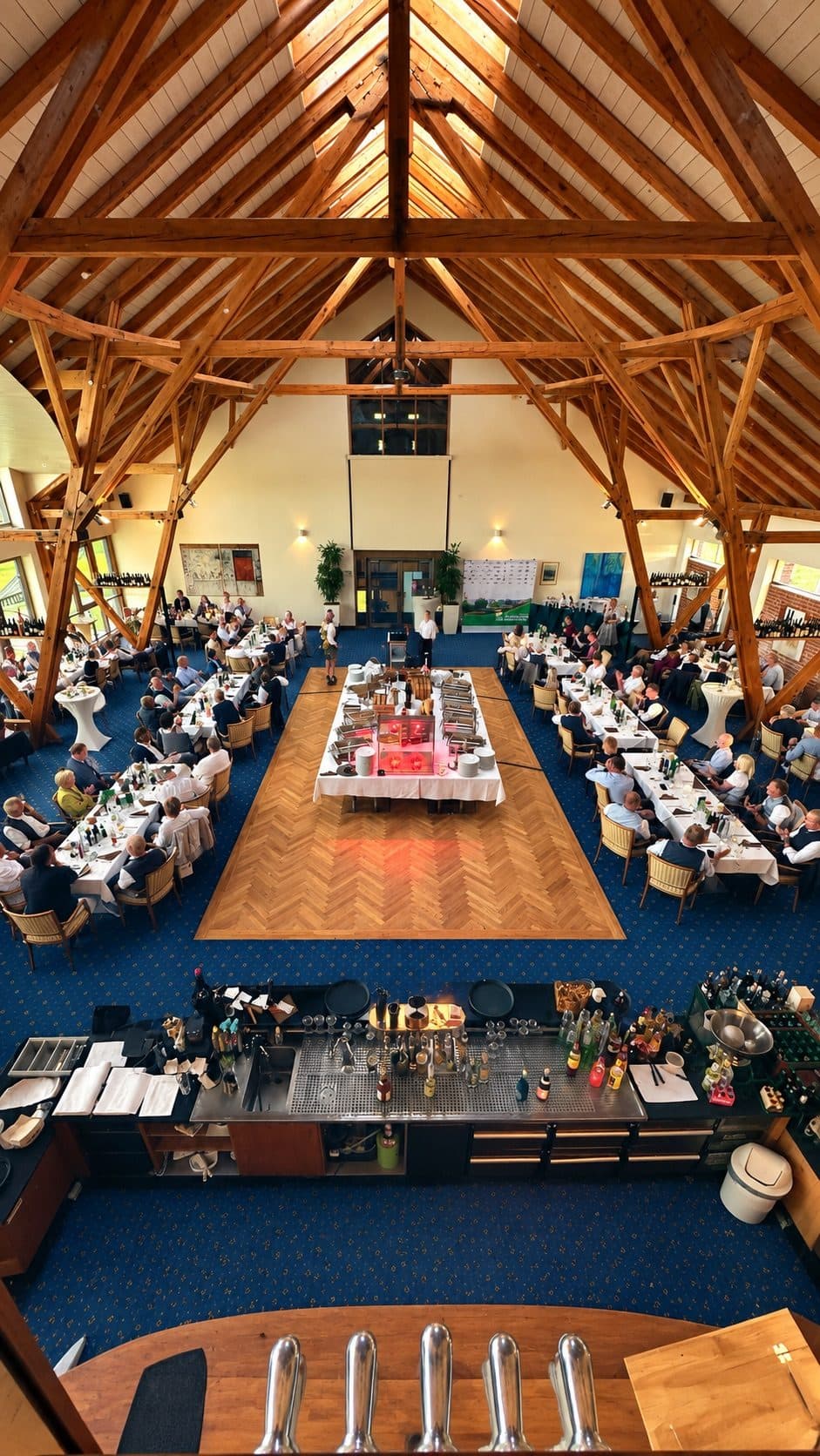 The hall full of guests at a celebration, seen from the gallery, with long tables around a dance floor