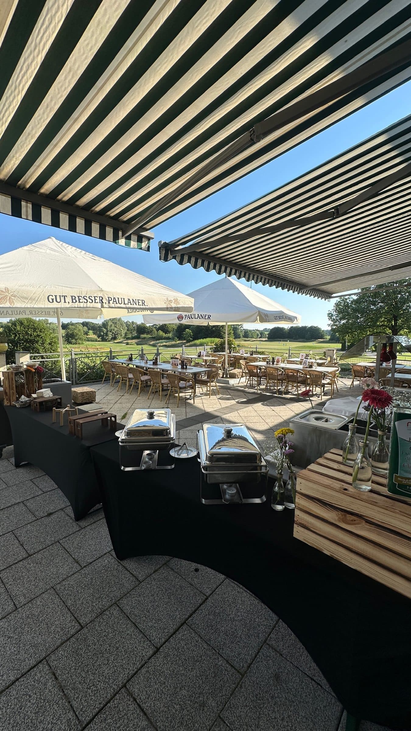 A buffet set out beneath the awning on the terrace, with a long table and the golf course behind